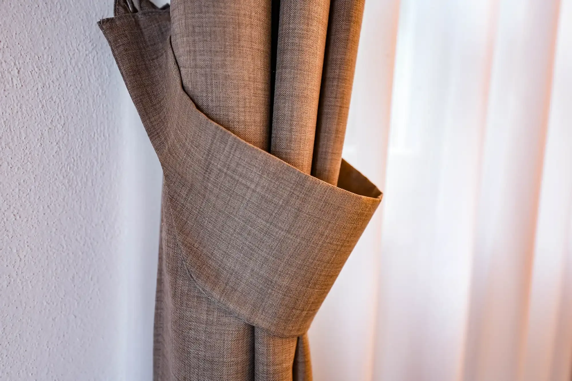 Brązowa zasłona przewiązana materiałową opaską przy oknie