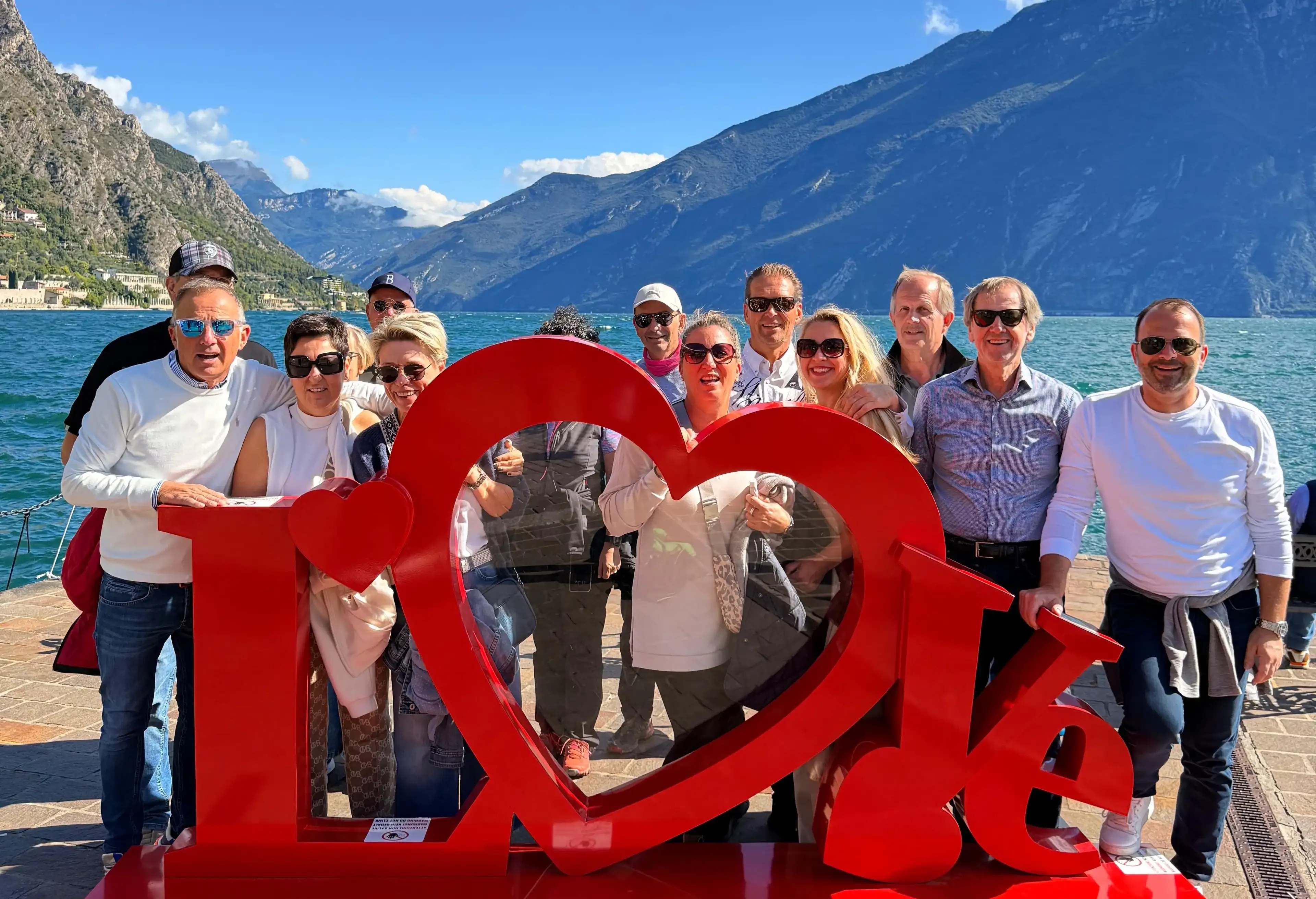 Groupe de touristes devant une sculpture rouge en cœur au bord d'un lac de montagne