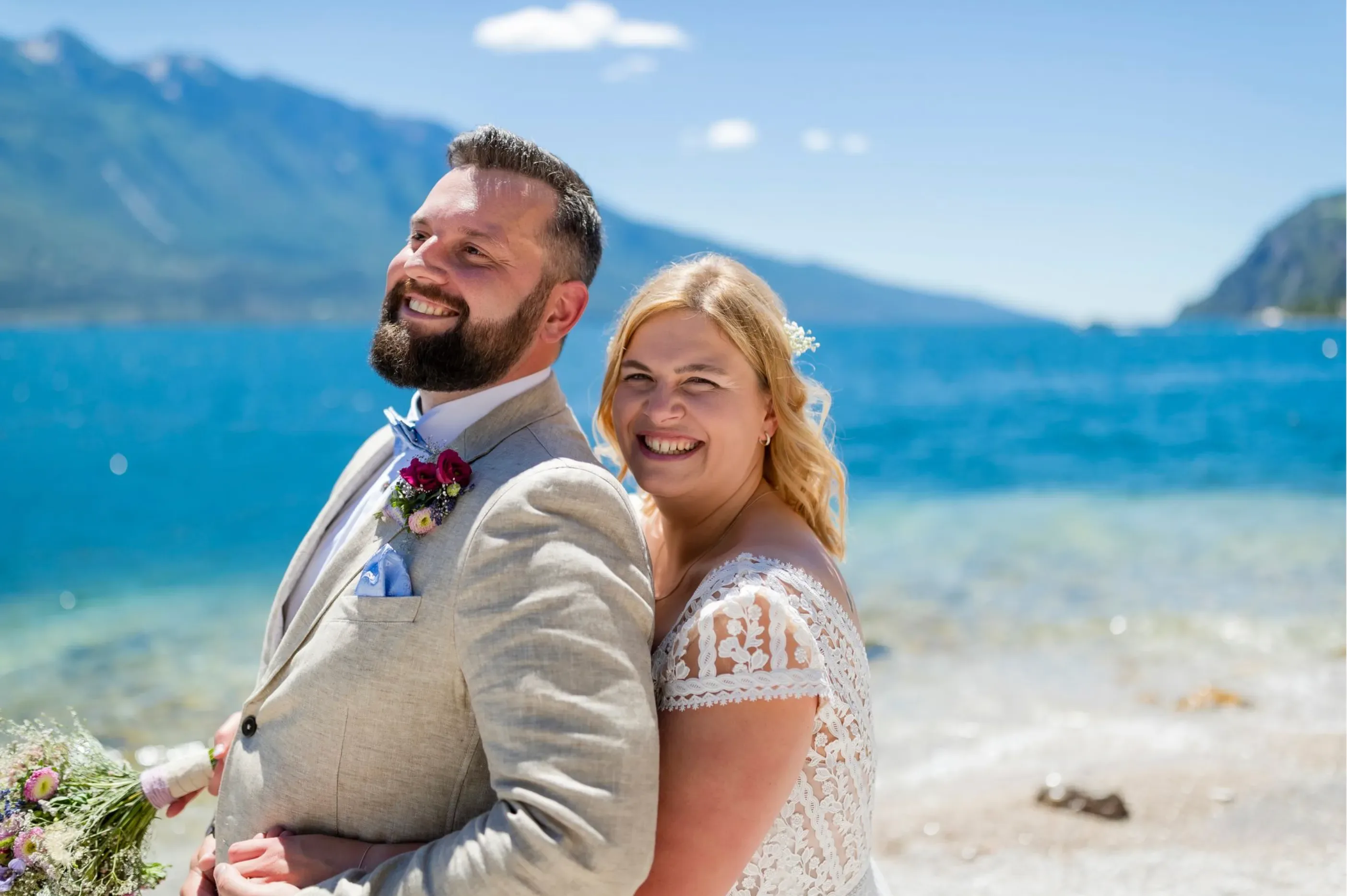 Smiling bride and groom embracing by the sea on a sunny day