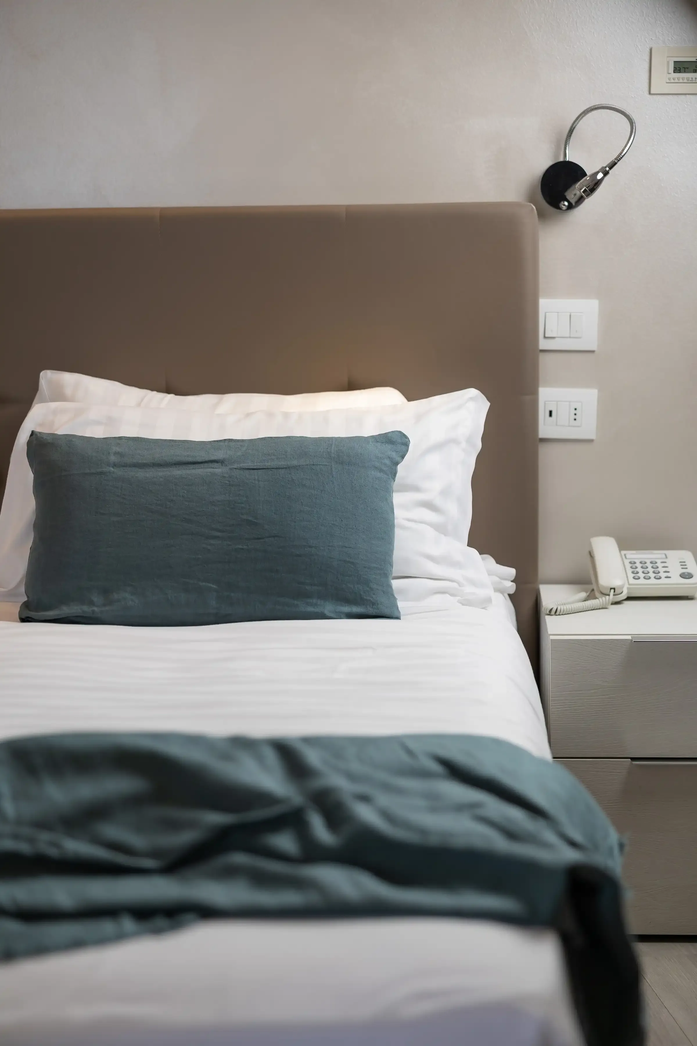 Łóżko pojedyncze z zieloną poduszką i białą szafką nocną w pokoju hotelowym