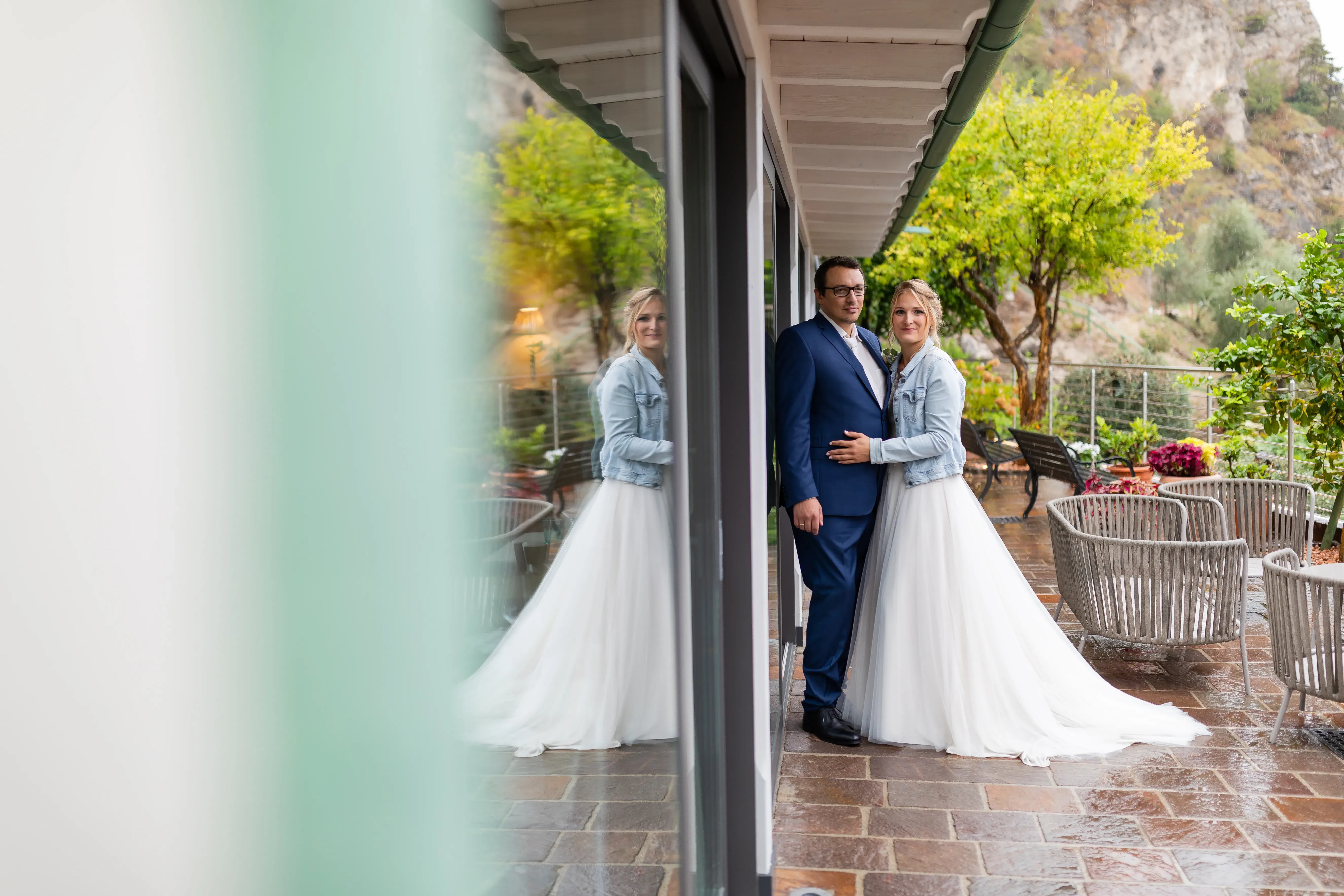 Wedding couple on a rainy terrace, bride in denim jacket and white dress